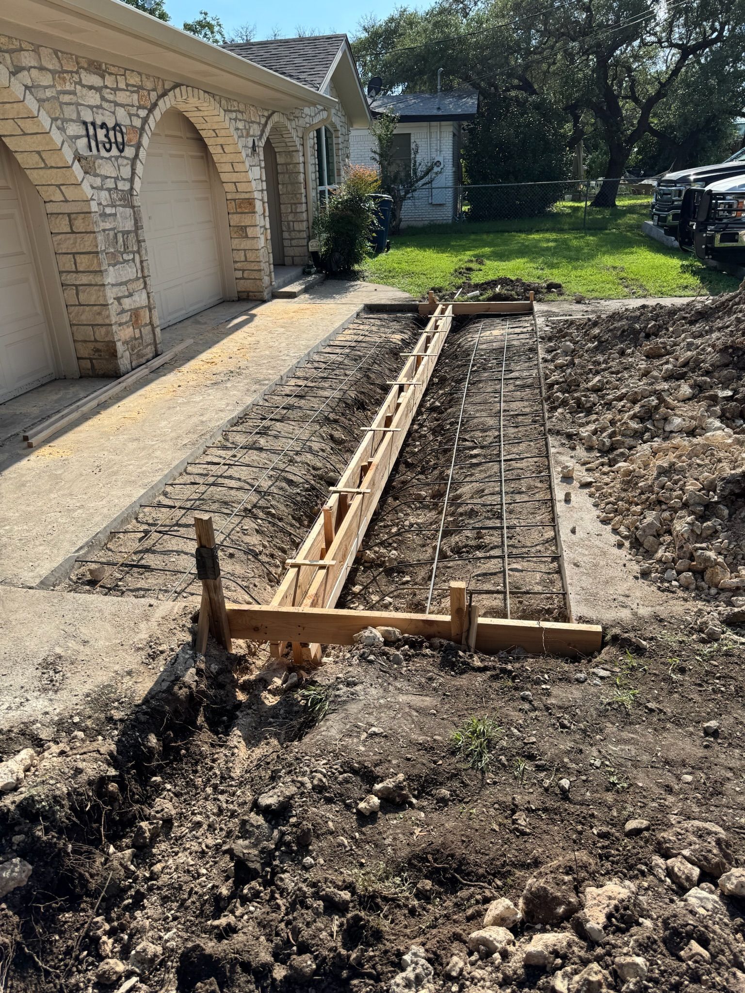Driveway construction: wooden forms, rebar, and dirt.  House with arched garage doors in the background.