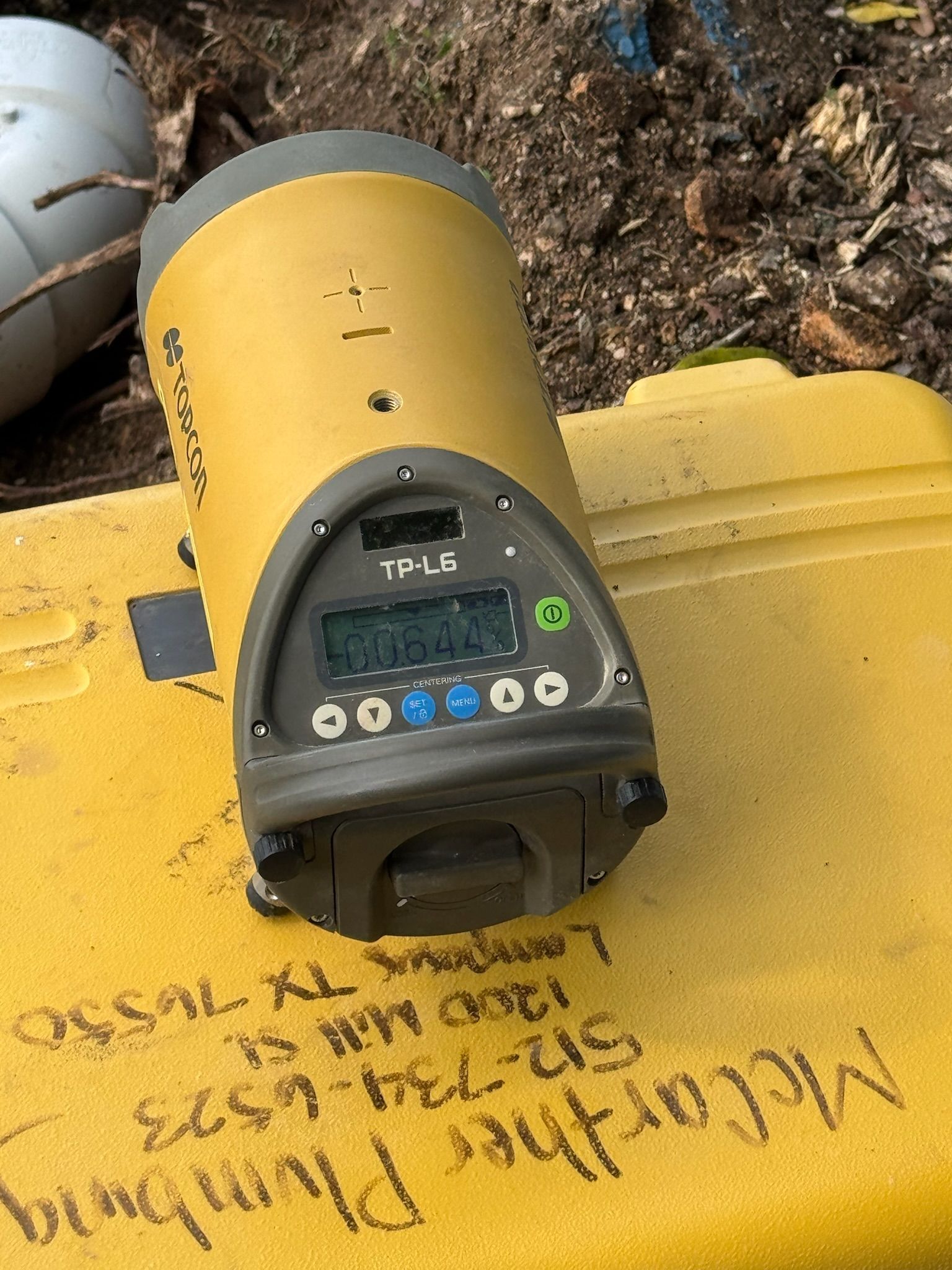 Yellow laser level on a yellow container, outdoors. It has a digital display.
