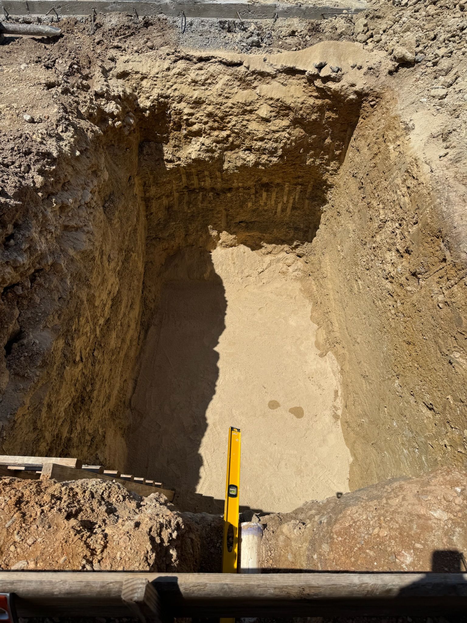 A deep construction pit, with a level leaned against the back wall.
