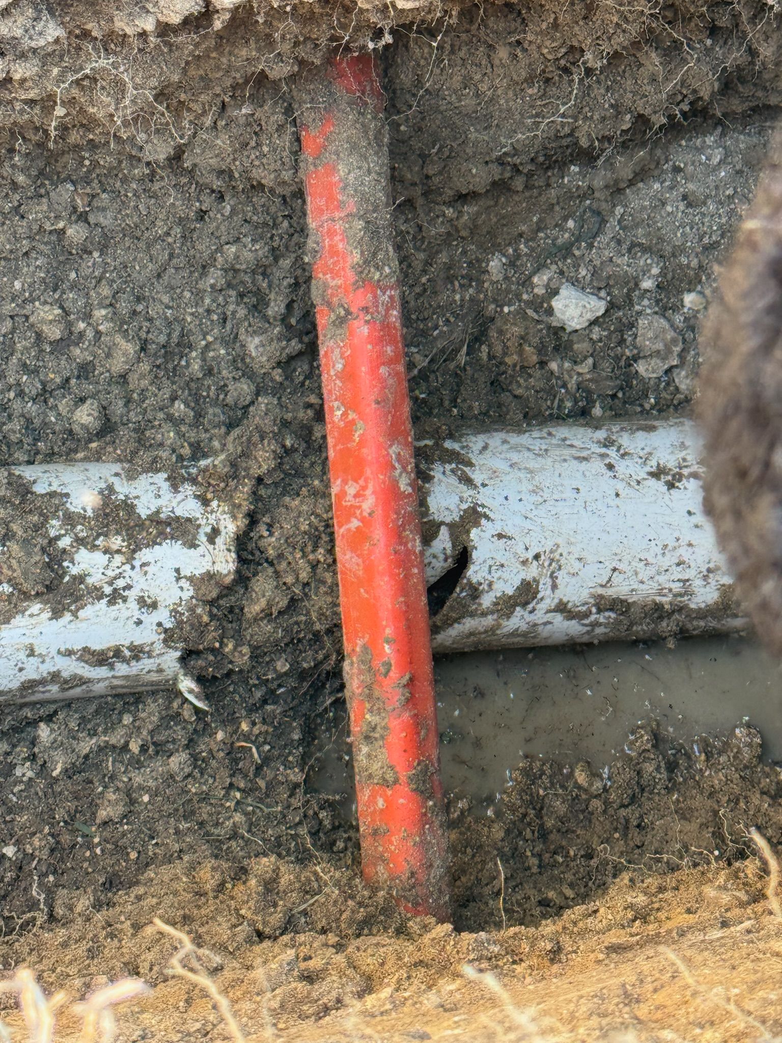Orange and white pipes in a dirt trench, with a small hole visible in the white pipe.