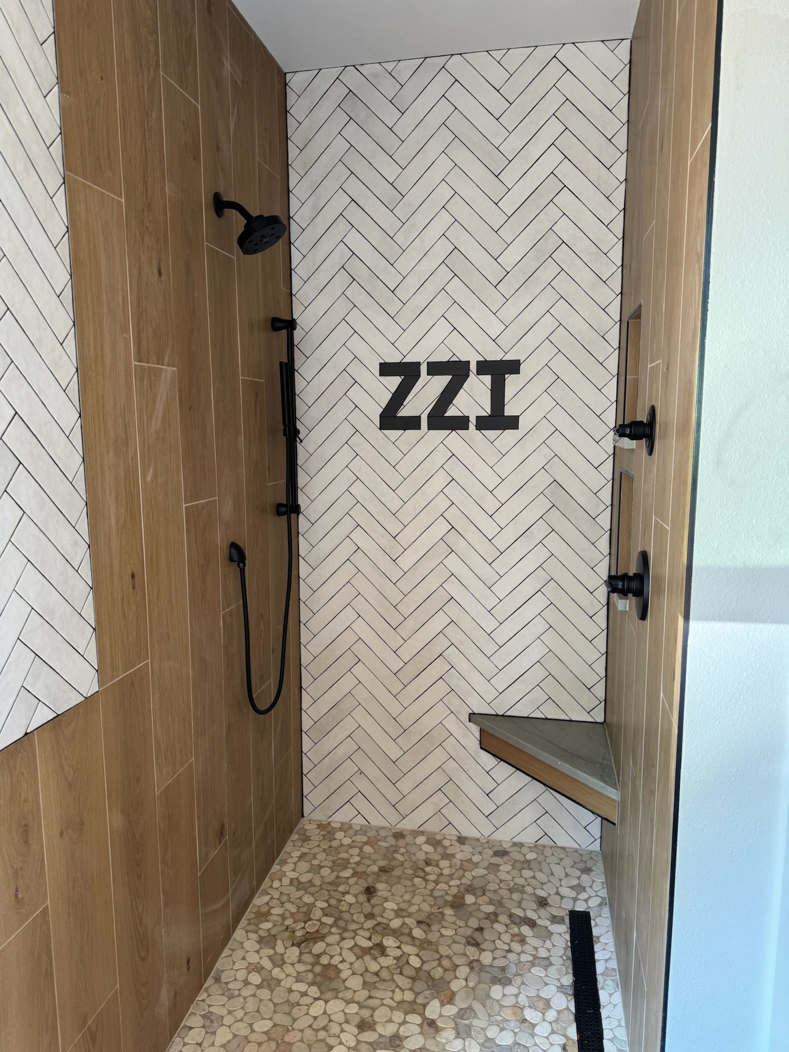 Modern shower with patterned tile and black fixtures. Features bench and 