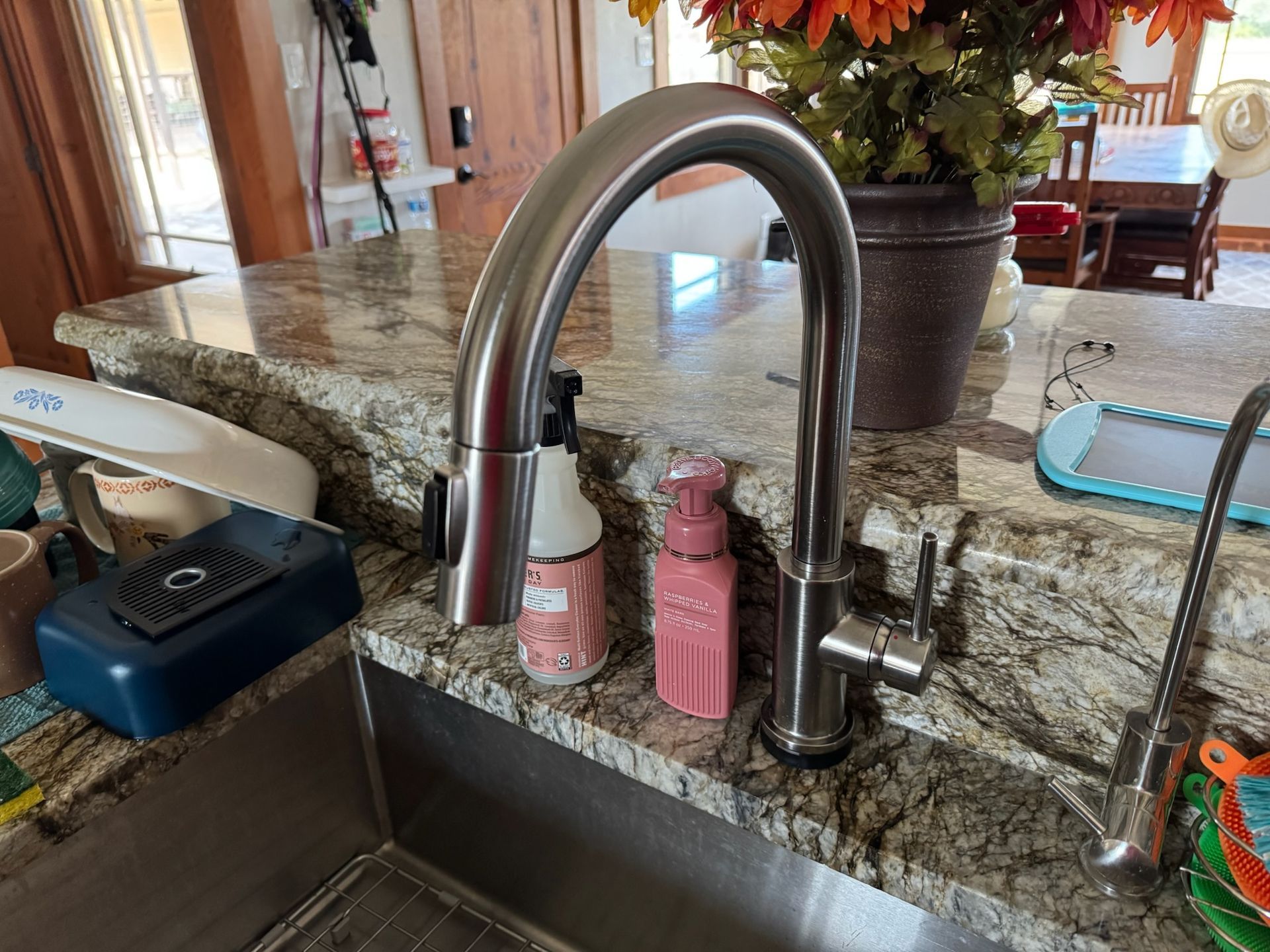 Stainless steel kitchen faucet with soap dispensers on a granite countertop.