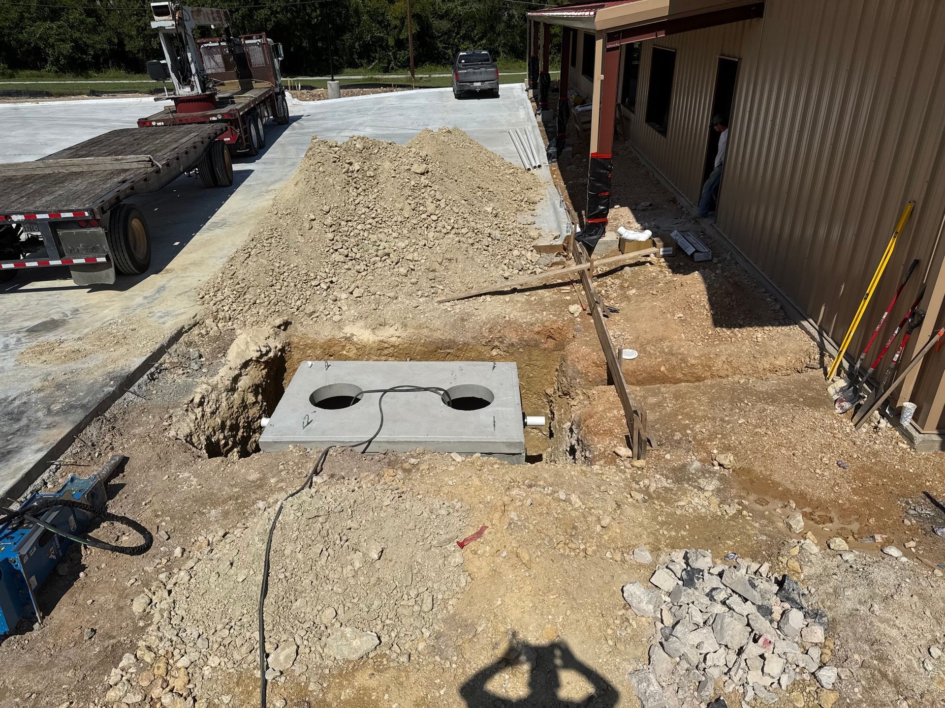 Construction site: a concrete box in an excavated area with gravel and building in the background.