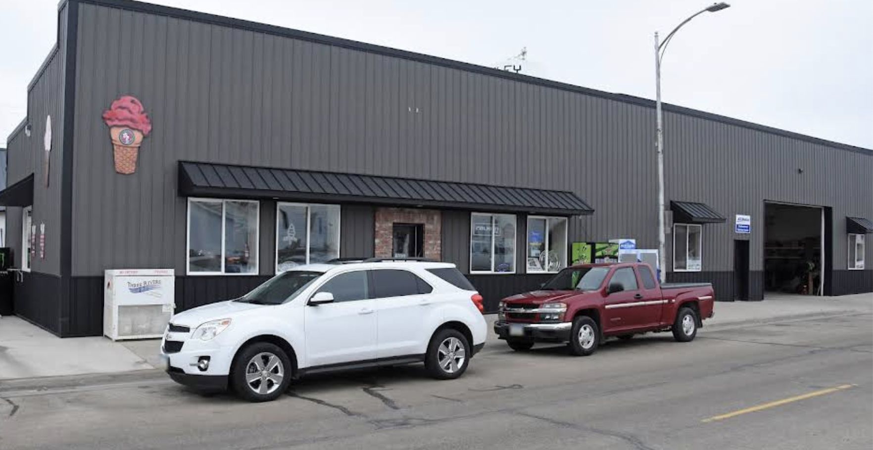 White SUV and red pickup truck parked in front of a dark gray building with ice cream cone sign.