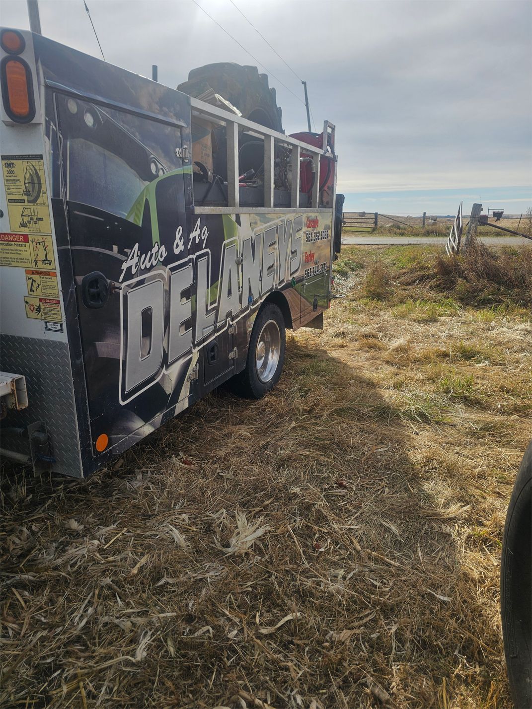 A tow truck with DELAN'S Auto & Gas branding parked on a grassy roadside, under a cloudy sky.