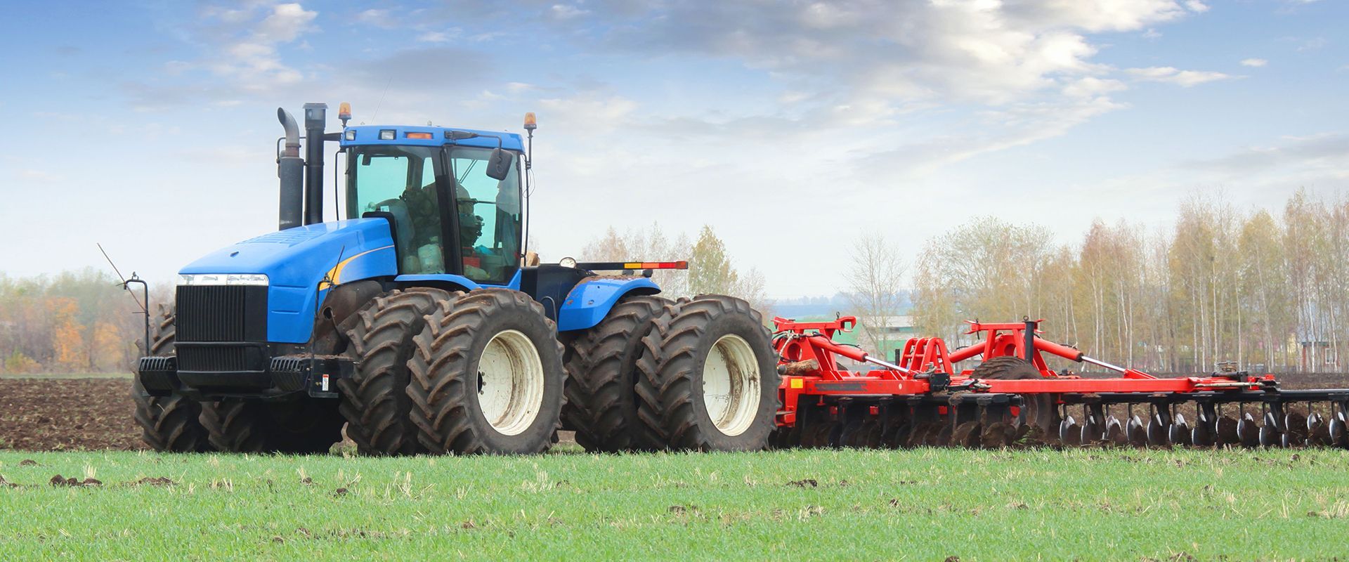 A blue tractor is plowing a field with a plow attached to it.