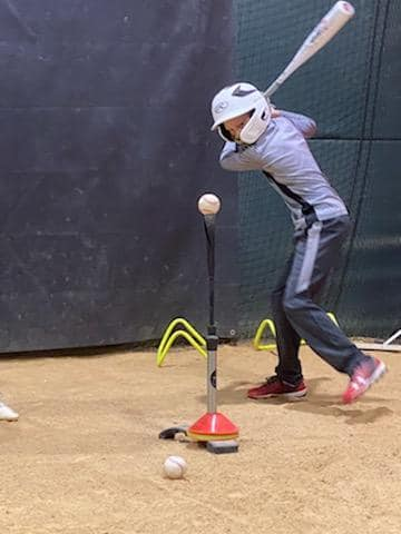A person is swinging a bat at a baseball on a tee.