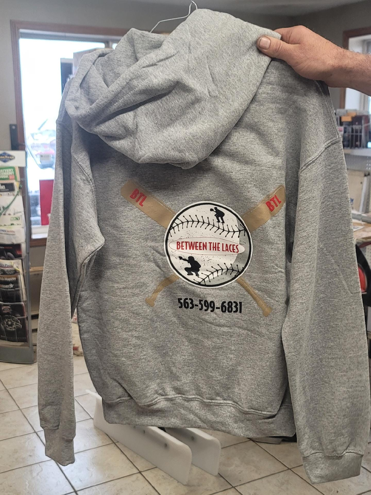A person is holding a gray hoodie with a baseball logo on it.