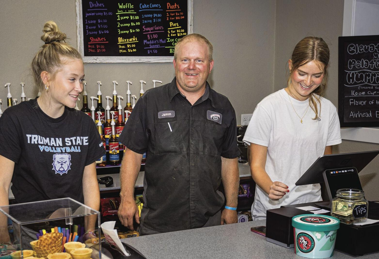 A man and two girls are standing behind a counter in a restaurant.
