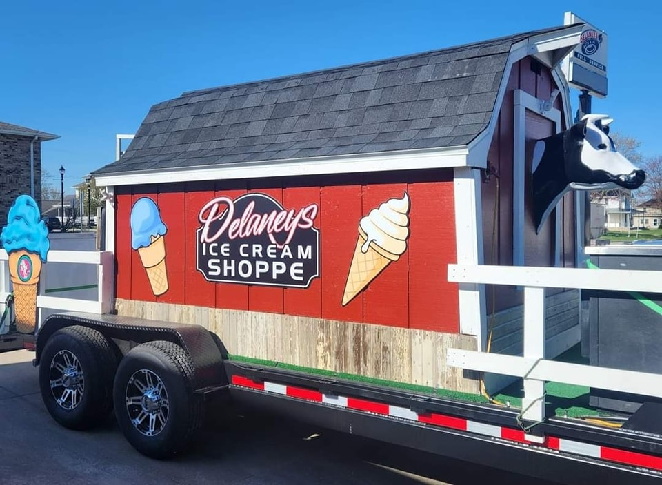 An ice cream shoppe trailer is parked in front of a red barn