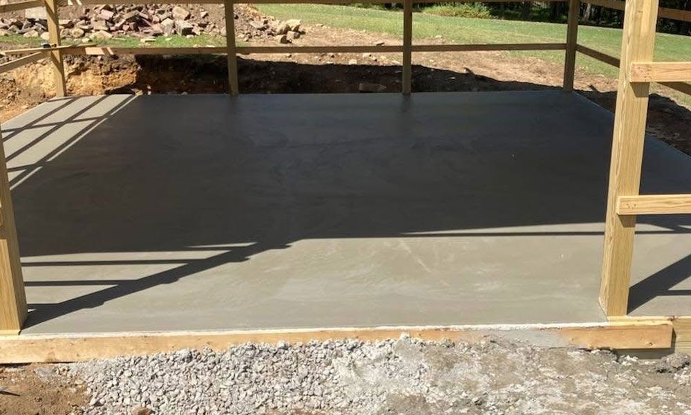 Wooden framed structure with a poured concrete floor, outdoors.