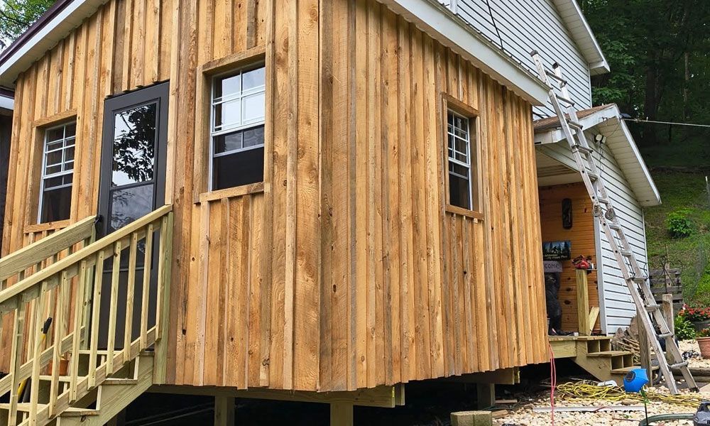 Wooden structure with steps and windows, attached to a white house.