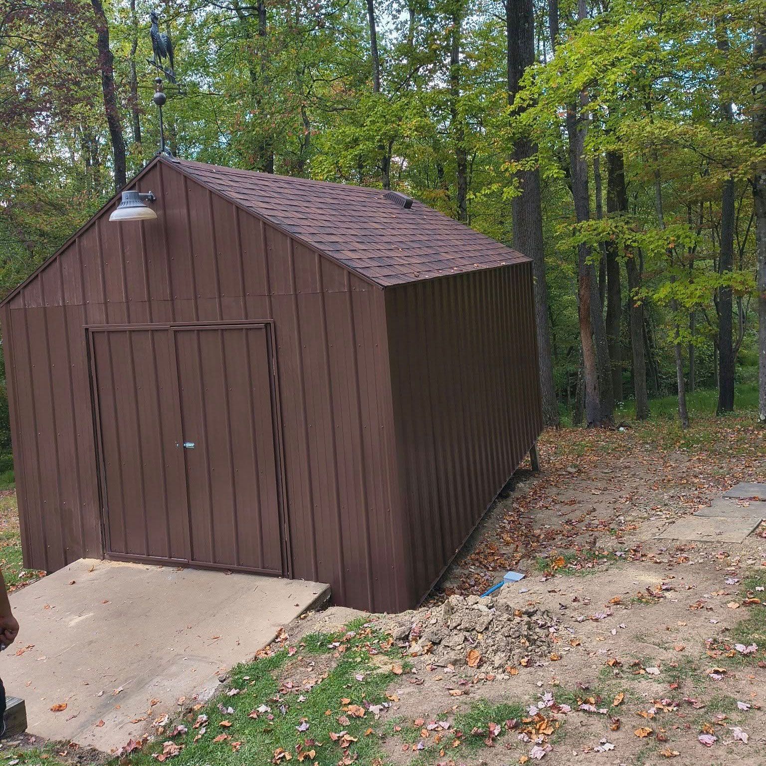 Brown shed with a concrete ramp in a wooded area.