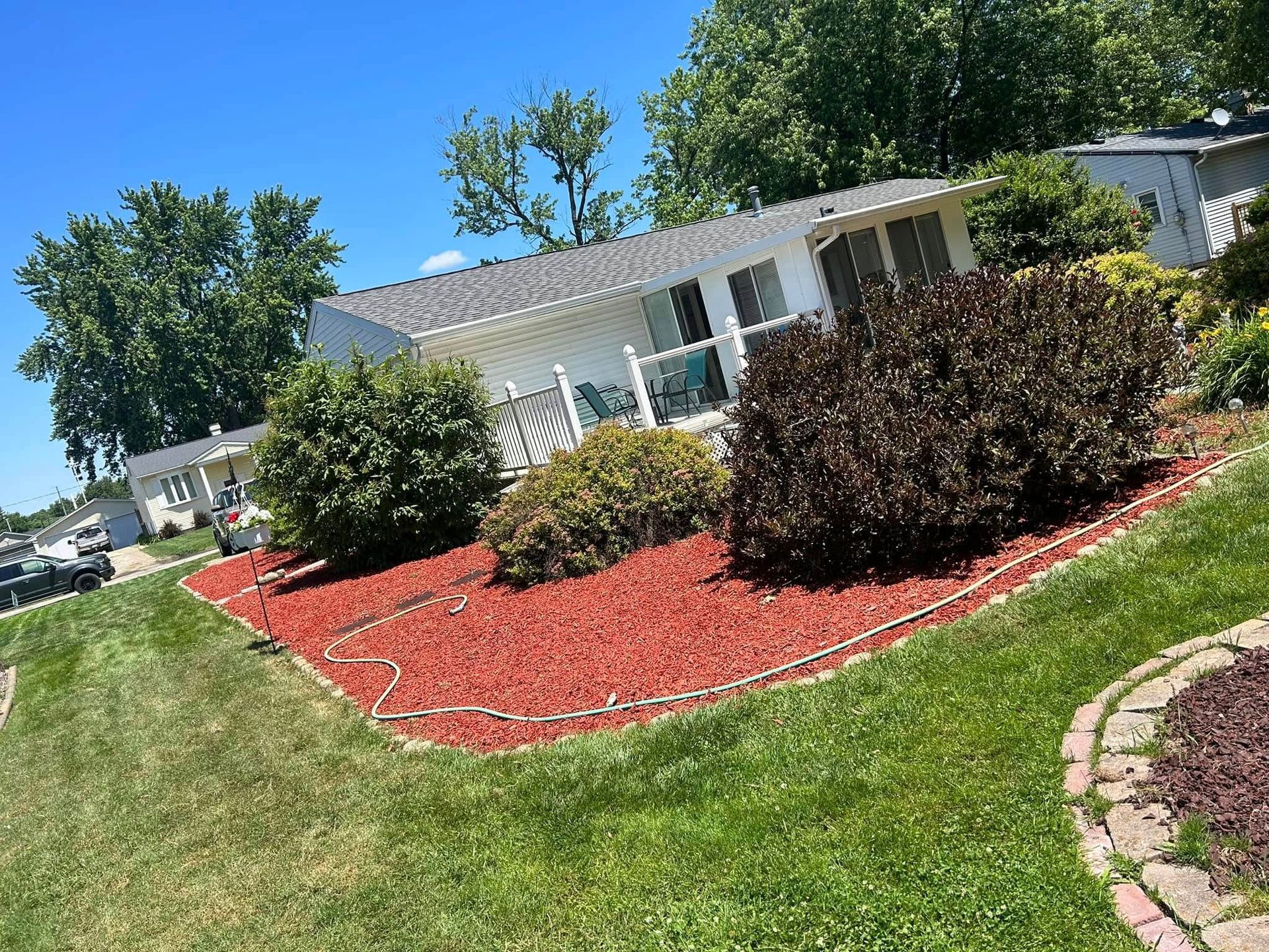 White house with red mulch and green bushes, under a bright blue sky.