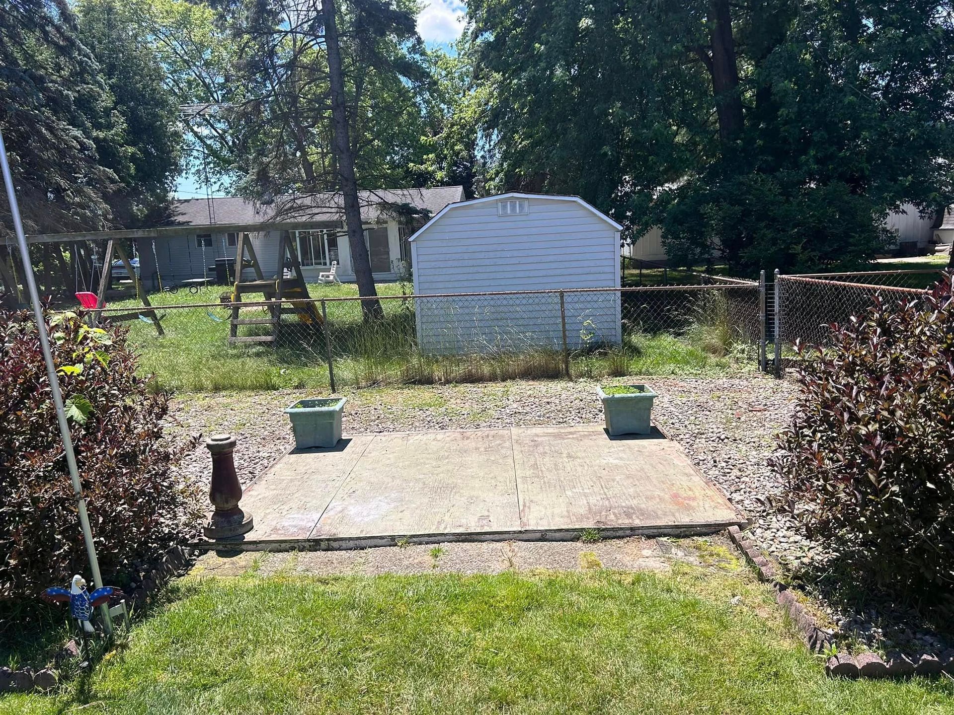 A backyard patio with a shed in the center and swing set in the background.