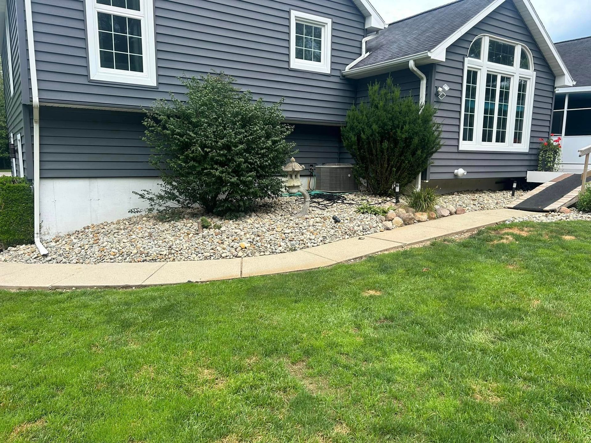 Gray house with a curved concrete walkway, rock garden, and green lawn.