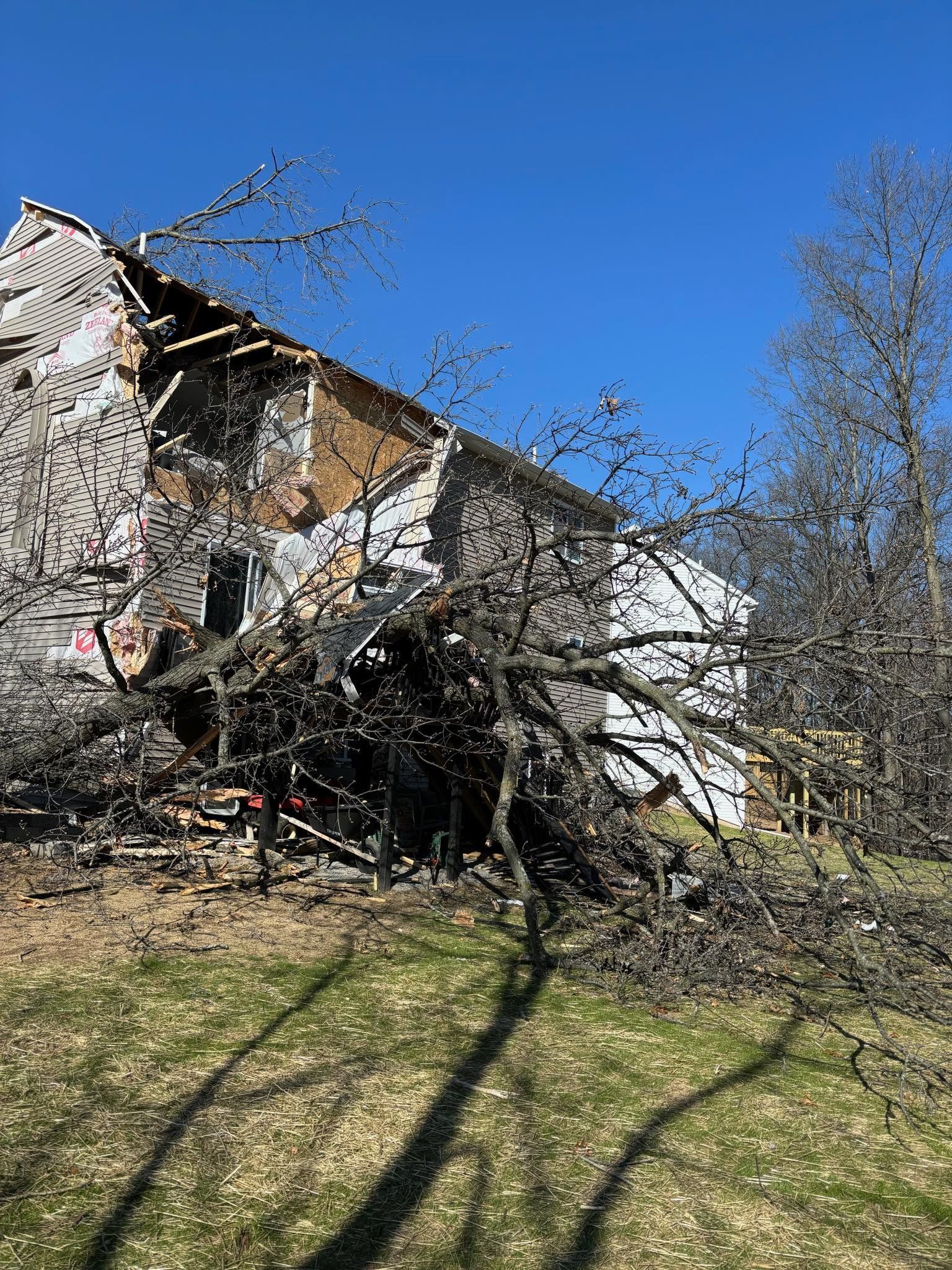 Damaged building with exposed interior, debris, and bare tree branches under a clear blue sky.