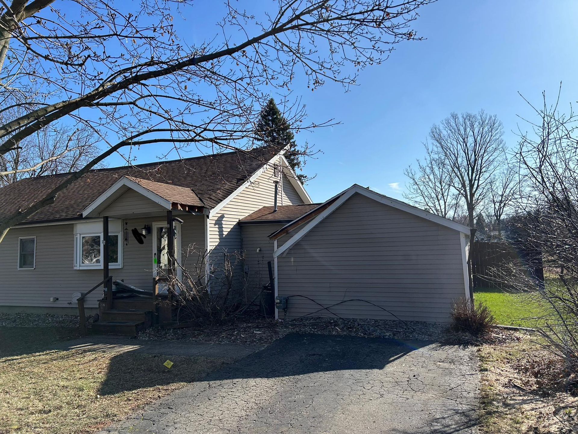 Beige house with a driveway and leafless trees under a blue sky.