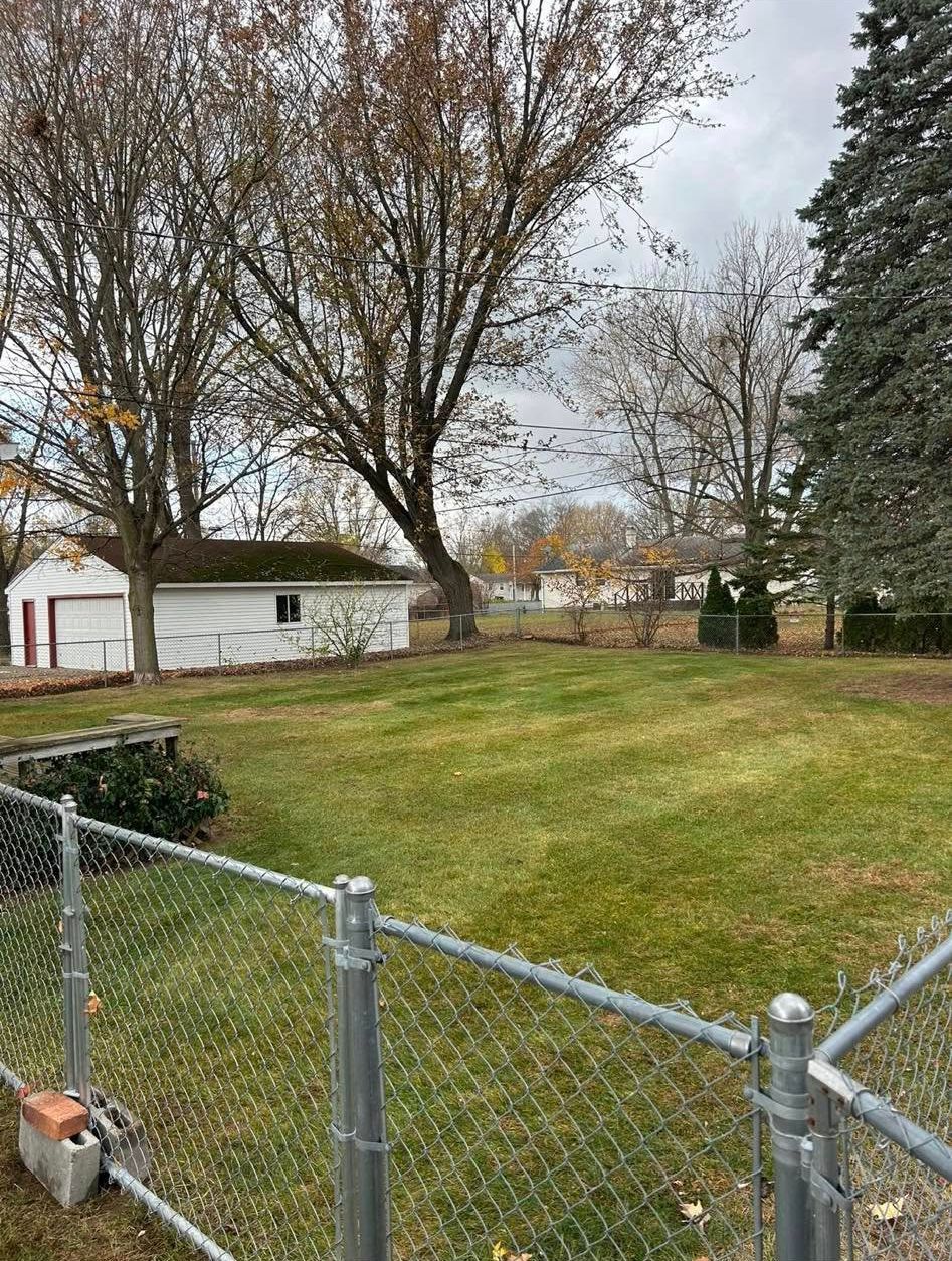 A backyard with a garage, trees, and a chain-link fence under an overcast sky.