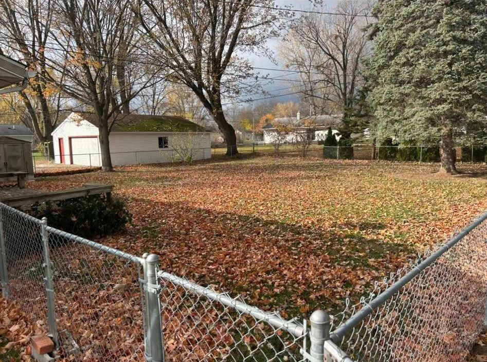 Backyard covered in brown leaves, with a chain-link fence in the foreground and a white garage in the distance.