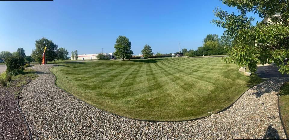 Green lawn with freshly cut stripes, gravel border, blue sky, trees.