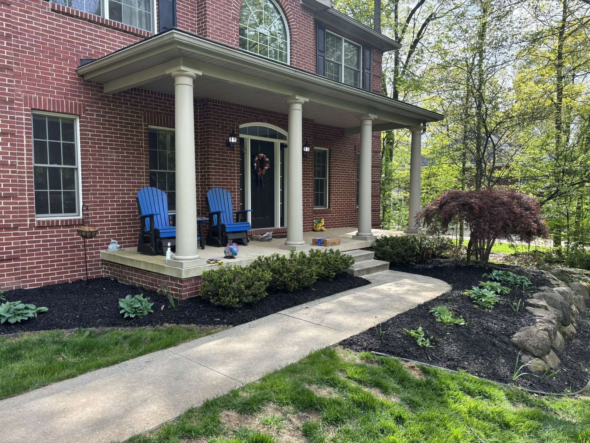 Red brick house with a porch, blue chairs, and a landscaped yard.