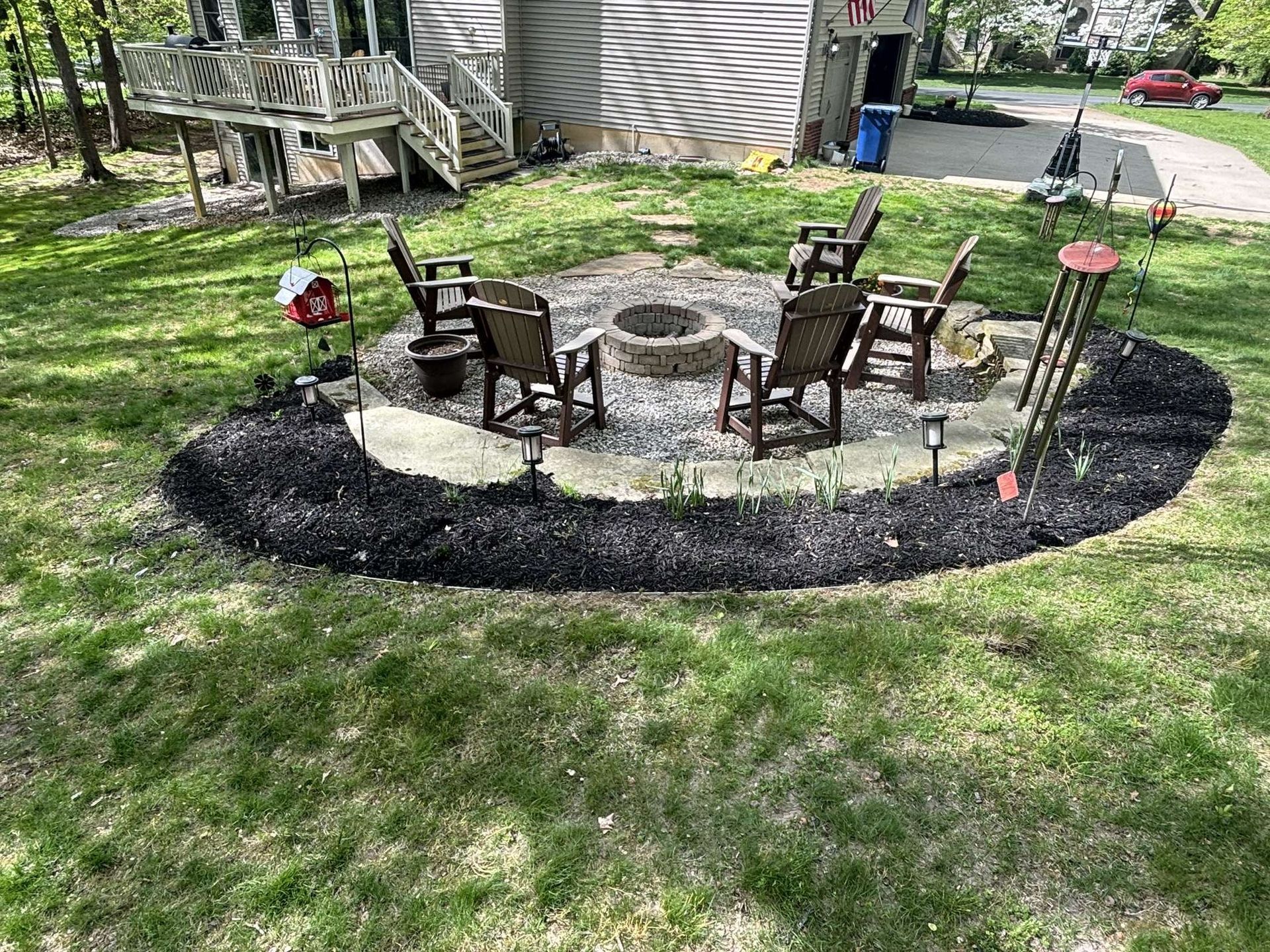 Fire pit seating area in a backyard with chairs and black mulch border.