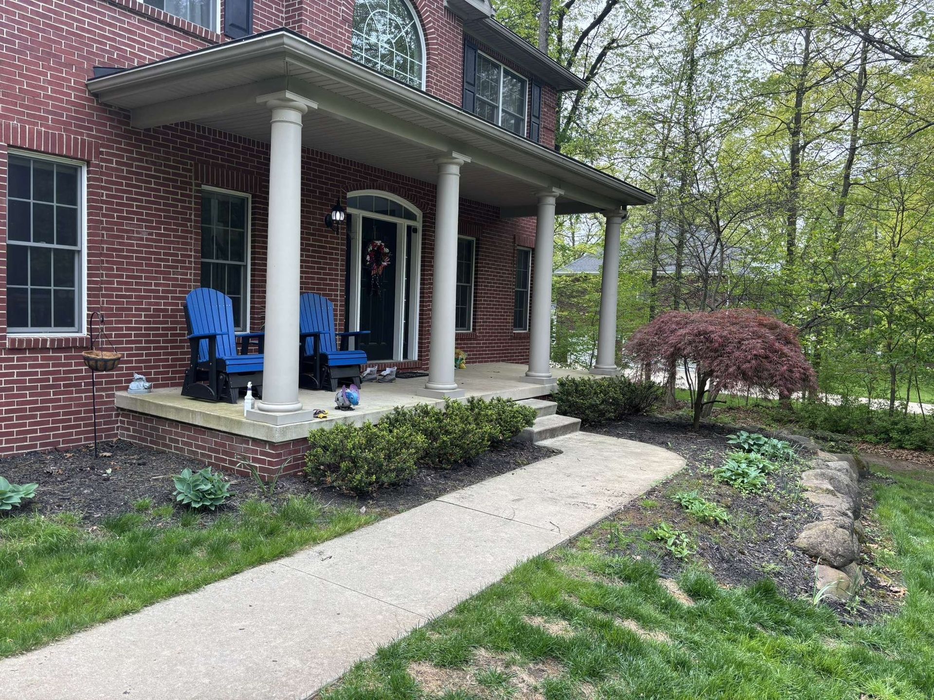 Red brick house with porch, white columns, blue chairs, and a curving walkway.
