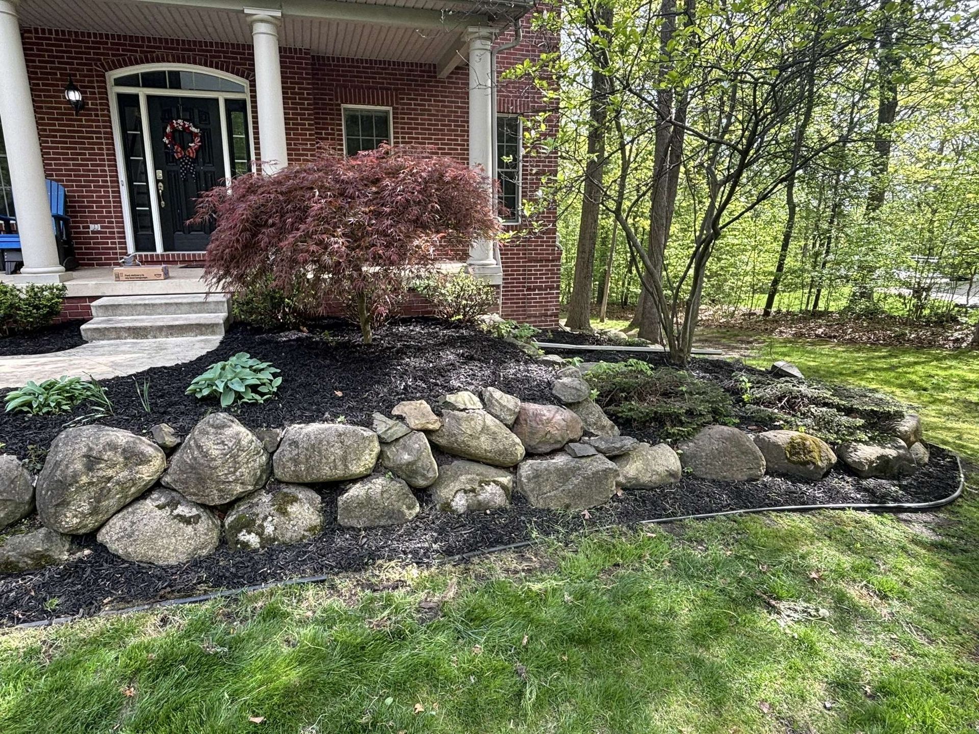 Stone retaining wall borders a mulched garden bed in front of a house.
