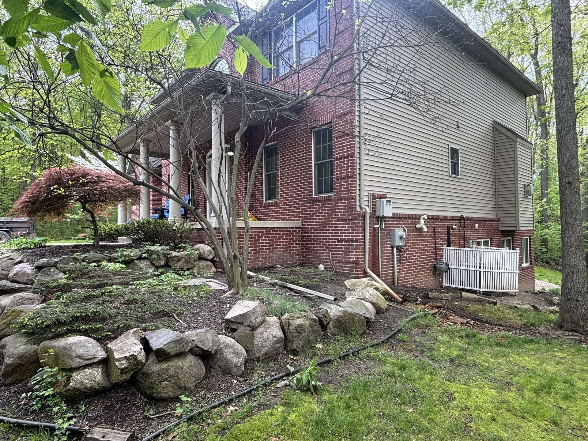 House with brick and siding, covered porch, stone retaining wall, and landscaping.