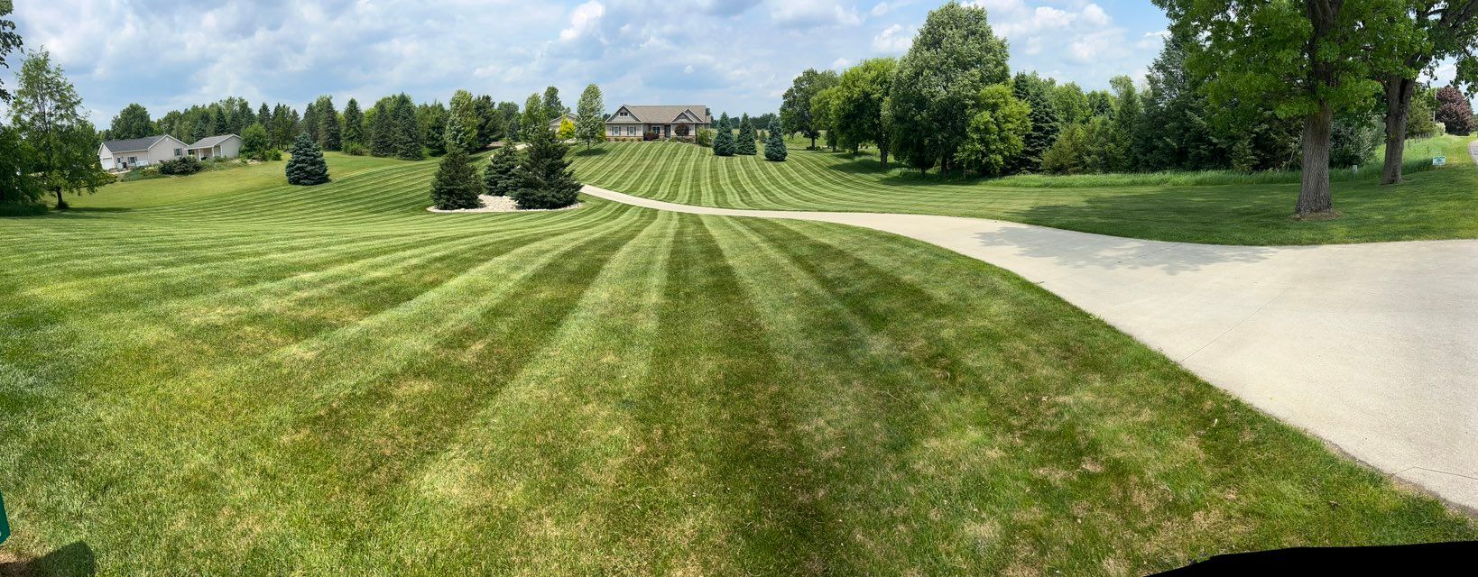 Lush green lawn with striped mowing pattern. A house is visible at the top of the hill.