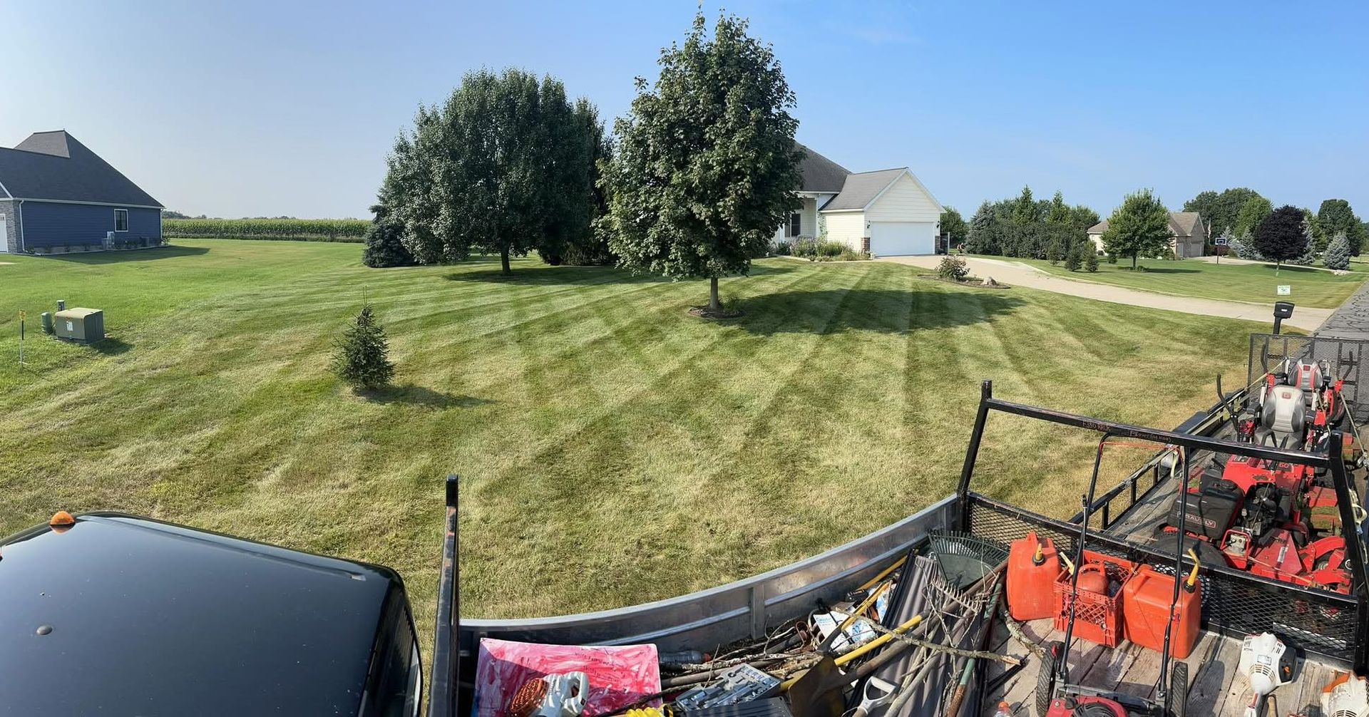 A truck bed loaded with equipment overlooks a freshly mowed lawn in a rural setting.