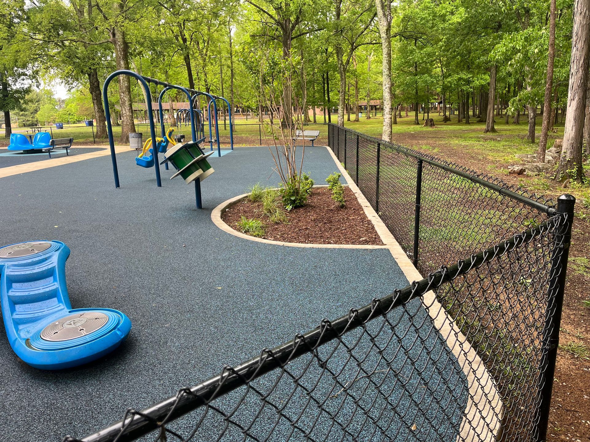 A chain link fence surrounds a playground in a park.