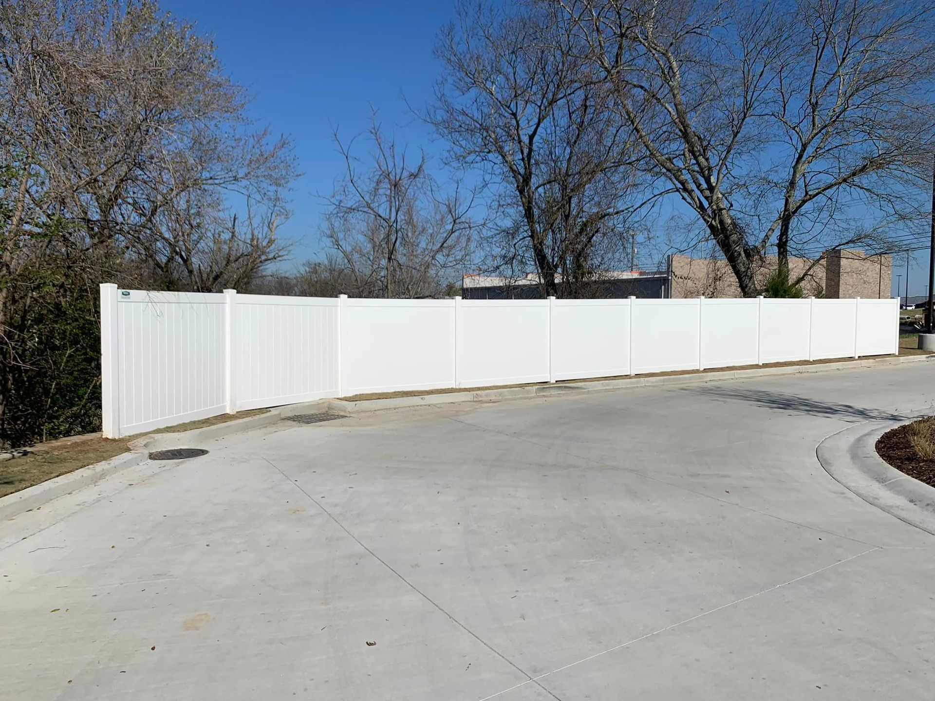 a white fence surrounds a concrete driveway with trees in the background
