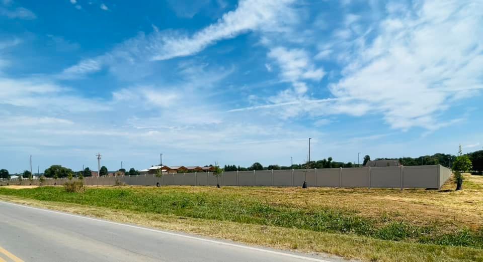 a large white fence surrounds a grassy field next to a road