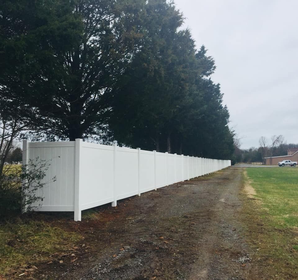 a white fence along a dirt road with trees in the background