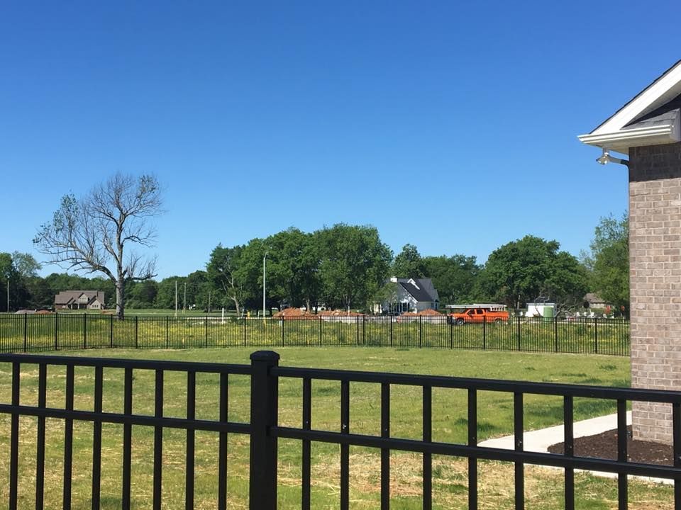 aluminum fence surrounds a grassy field in front of a house