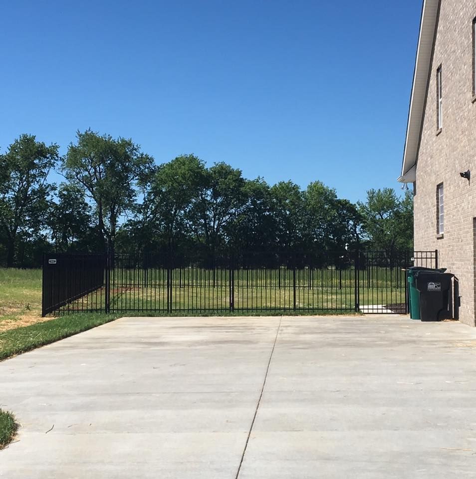 a concrete driveway with a fence and trees in the background