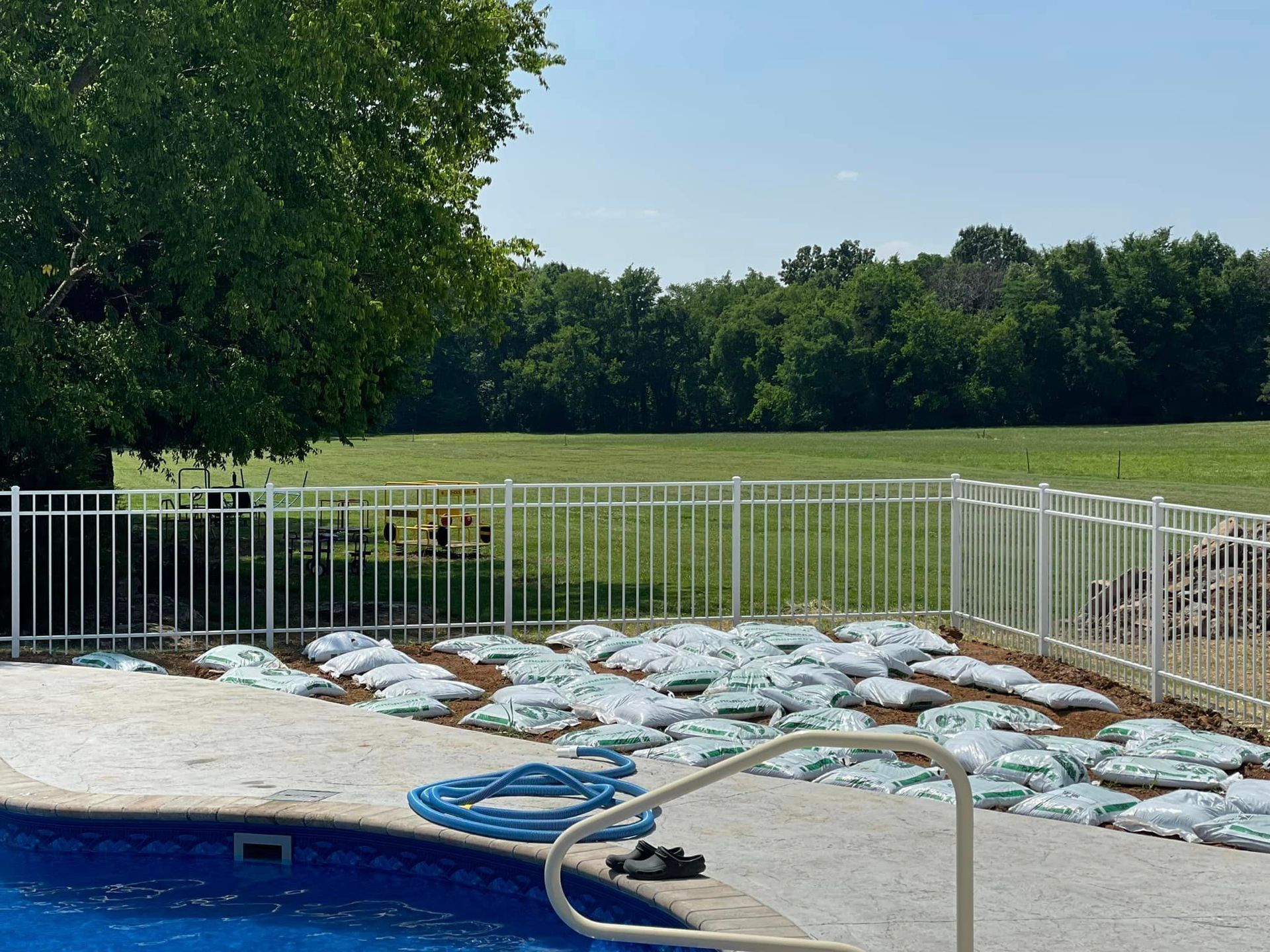 a swimming pool with a white aluminum fence surrounding it and a field in the background