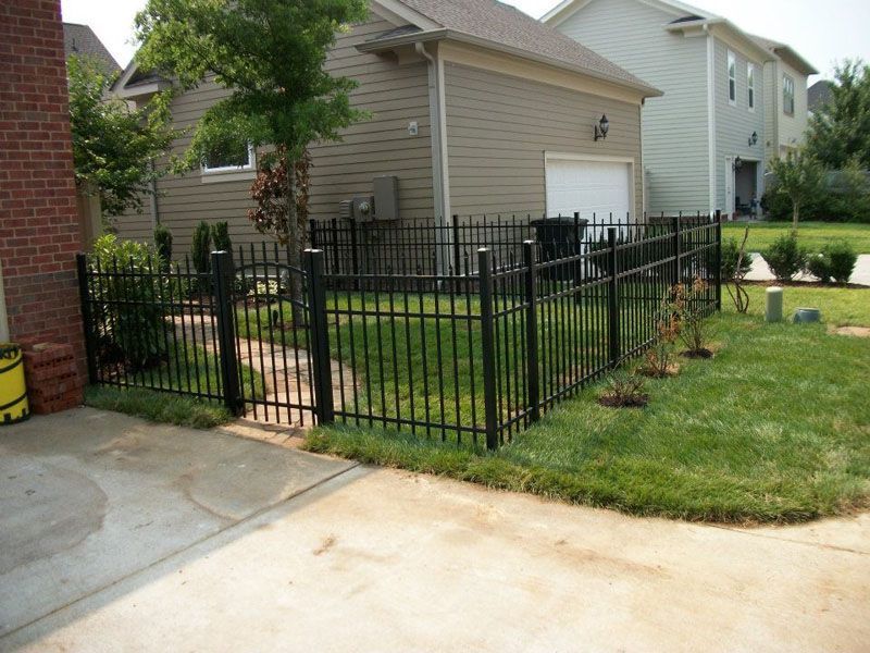 aluminum fence surrounds a lush green yard in front of a house