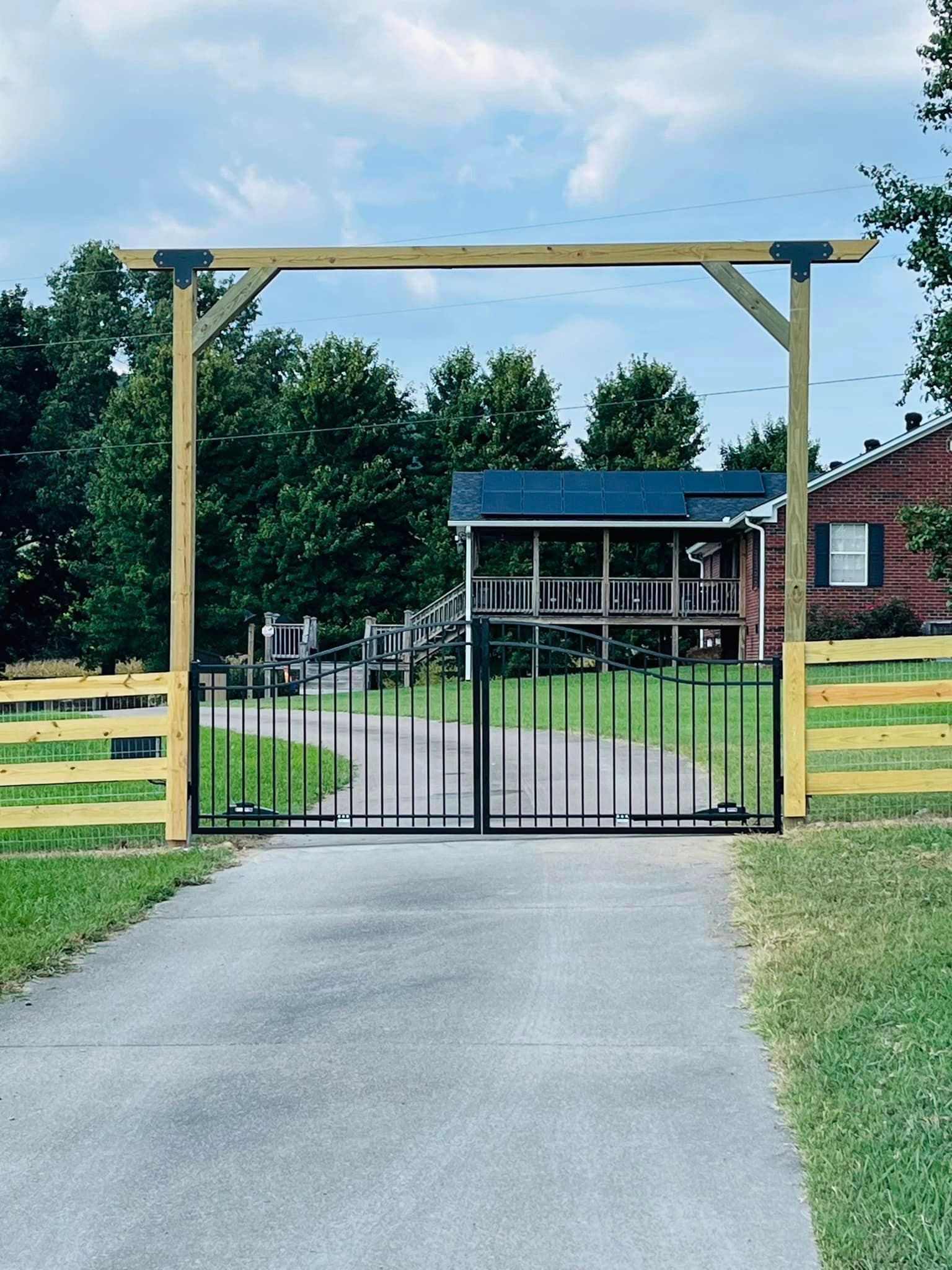 a driveway with a wooden fence and a metal gate leading to a house