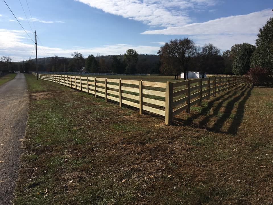 a long wooden fence surrounds a grassy field next to a road