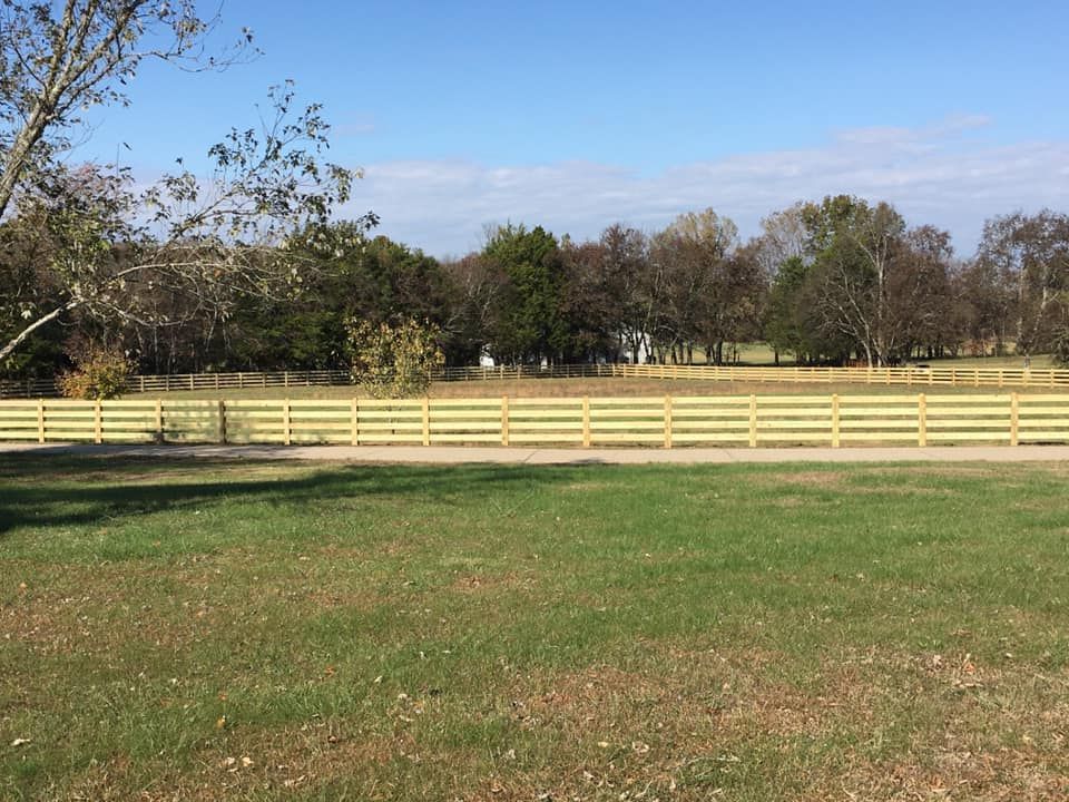 a wooden fence surrounds a grassy field with trees in the background