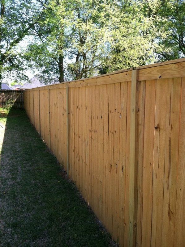 a long wooden fence is surrounded by trees in a backyard