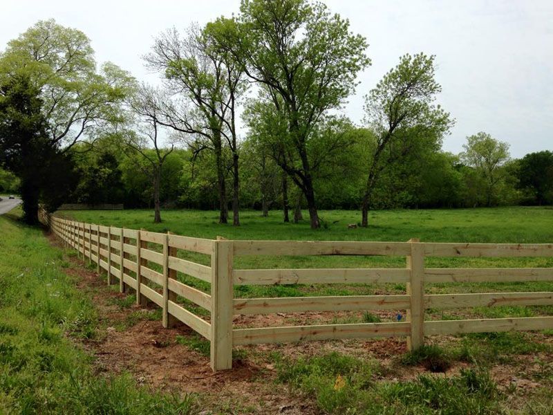 a wooden fence surrounds a grassy field with trees in the background