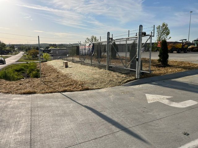 A white arrow is painted on the side of the road in front of a fence.