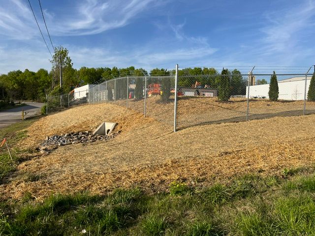 A fence surrounds a grassy hill with a building in the background.