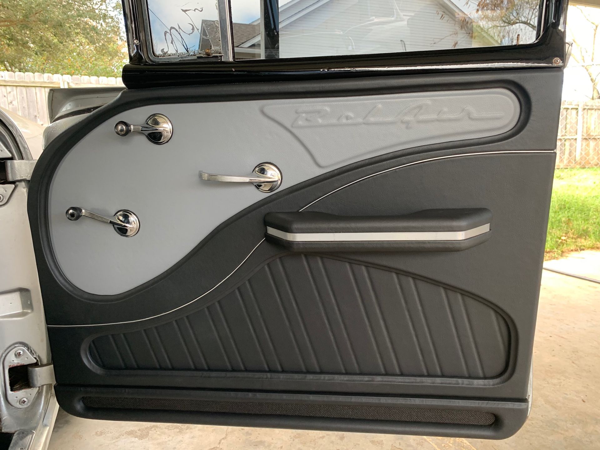 Custom car door panel with gray and black leather, chrome handles, and decorative stitching.