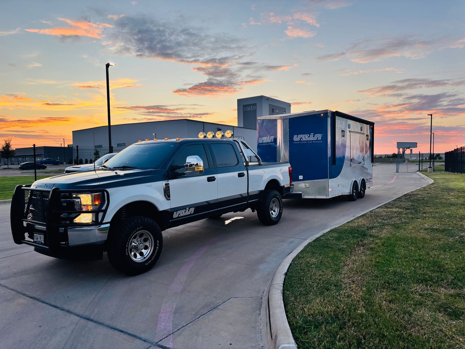 White and dark blue truck towing a matching trailer on a curved road at dusk.