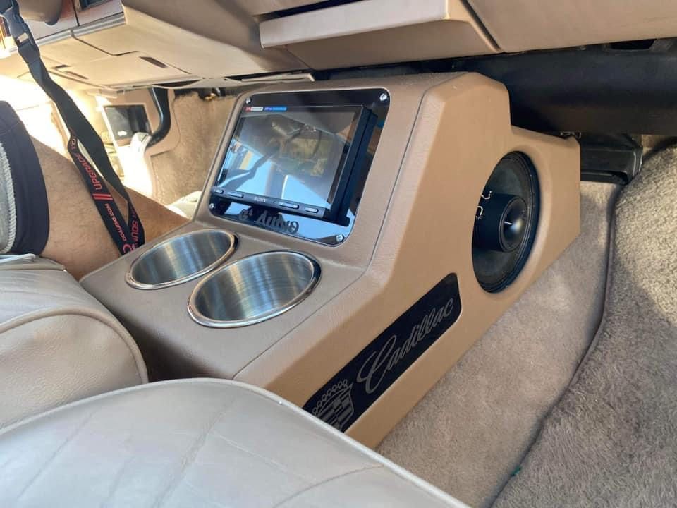 Custom car console with audio equipment, cup holders, and a screen; tan interior.